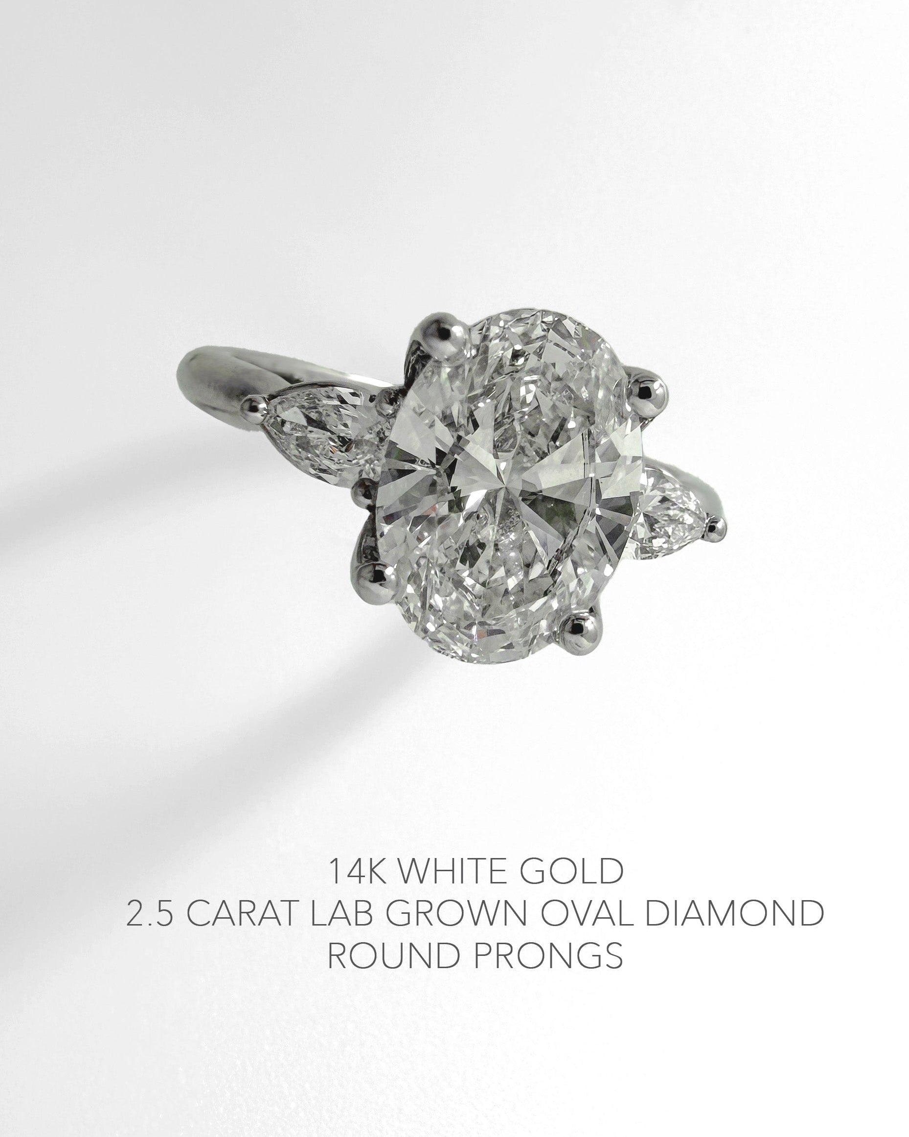 A 14k white gold ring featuring a 2.5 carat lab-grown oval diamond with round prongs and pear-cut side diamonds, shown on a clean white background with descriptive text below.